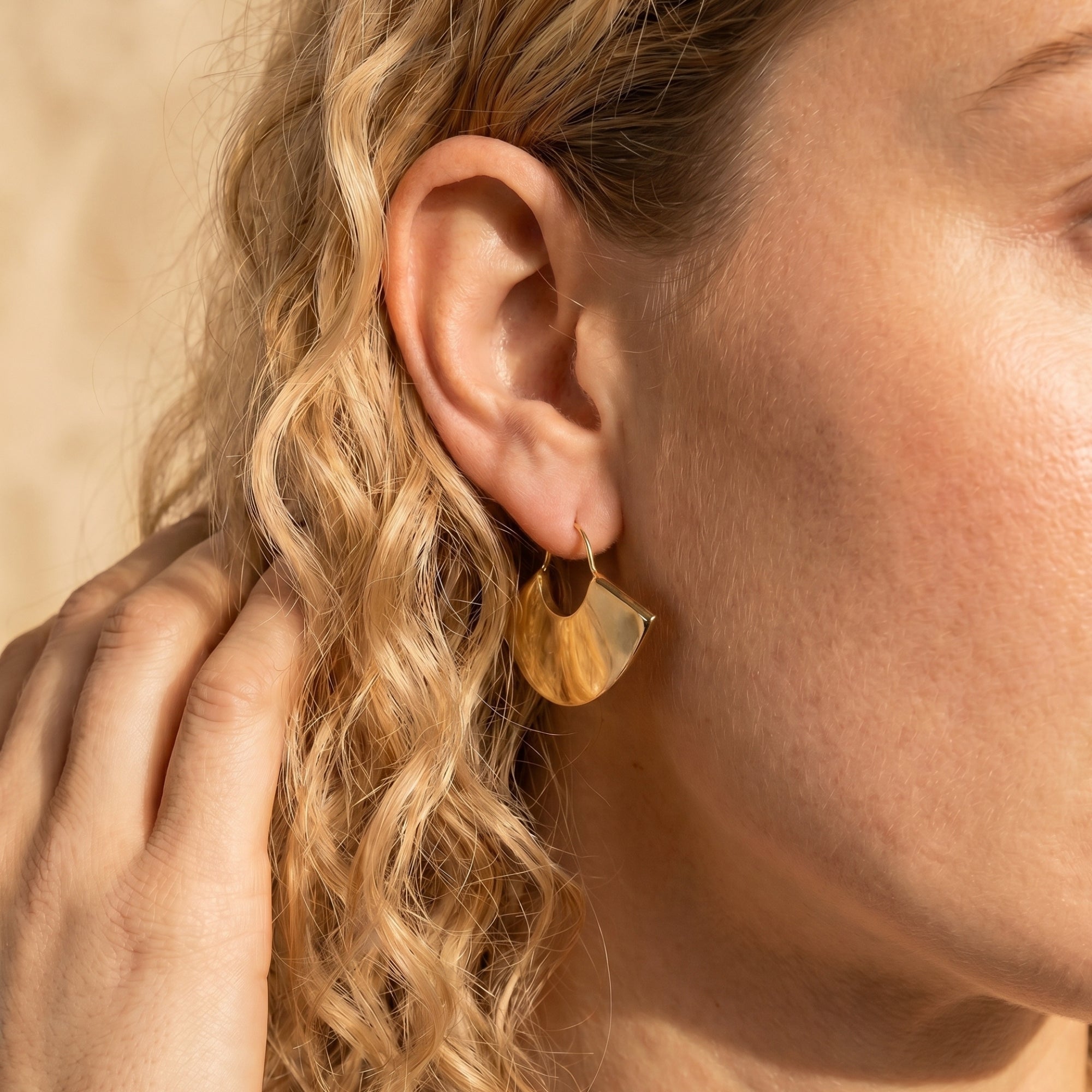 Close-up of a gold fan earring in 18K gold PVD stainless steel worn on an ear.