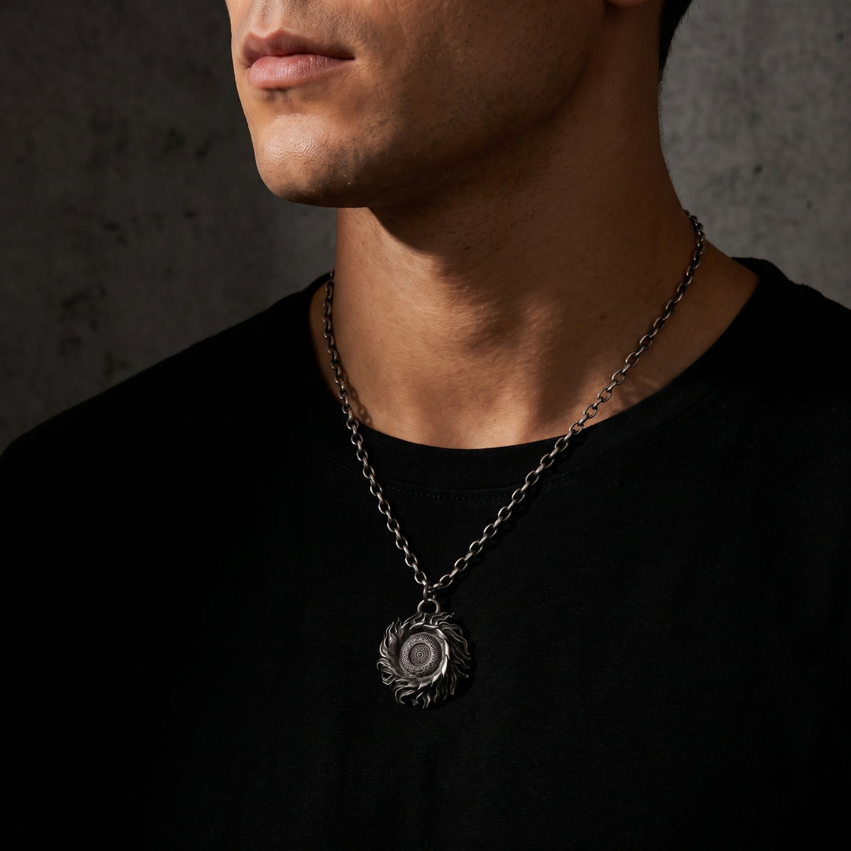 Wider model shot showing the silver solar flare pendant resting mid-chest on a black shirt.