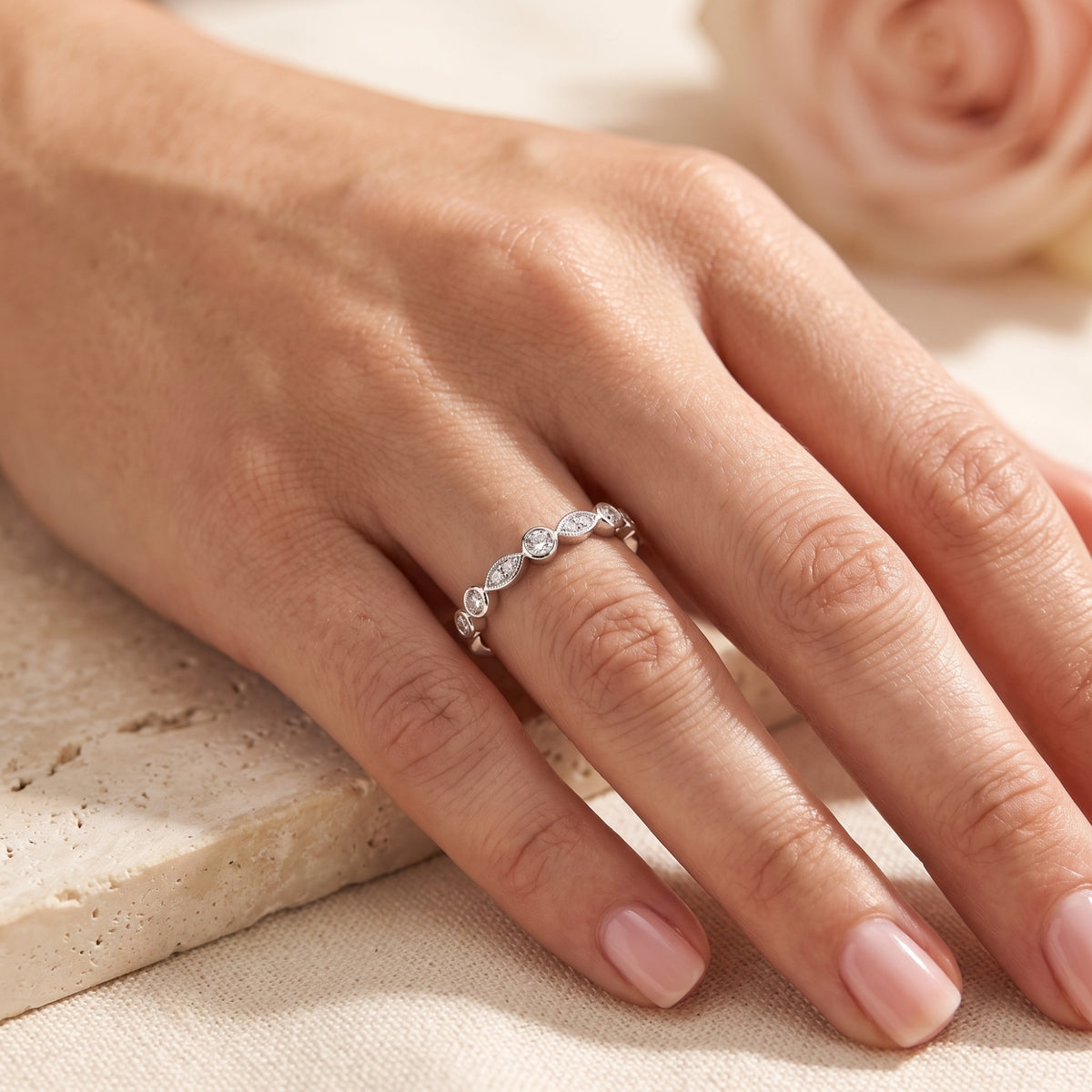Sterling silver cubic zirconia promise ring on a model's finger with a rose background.