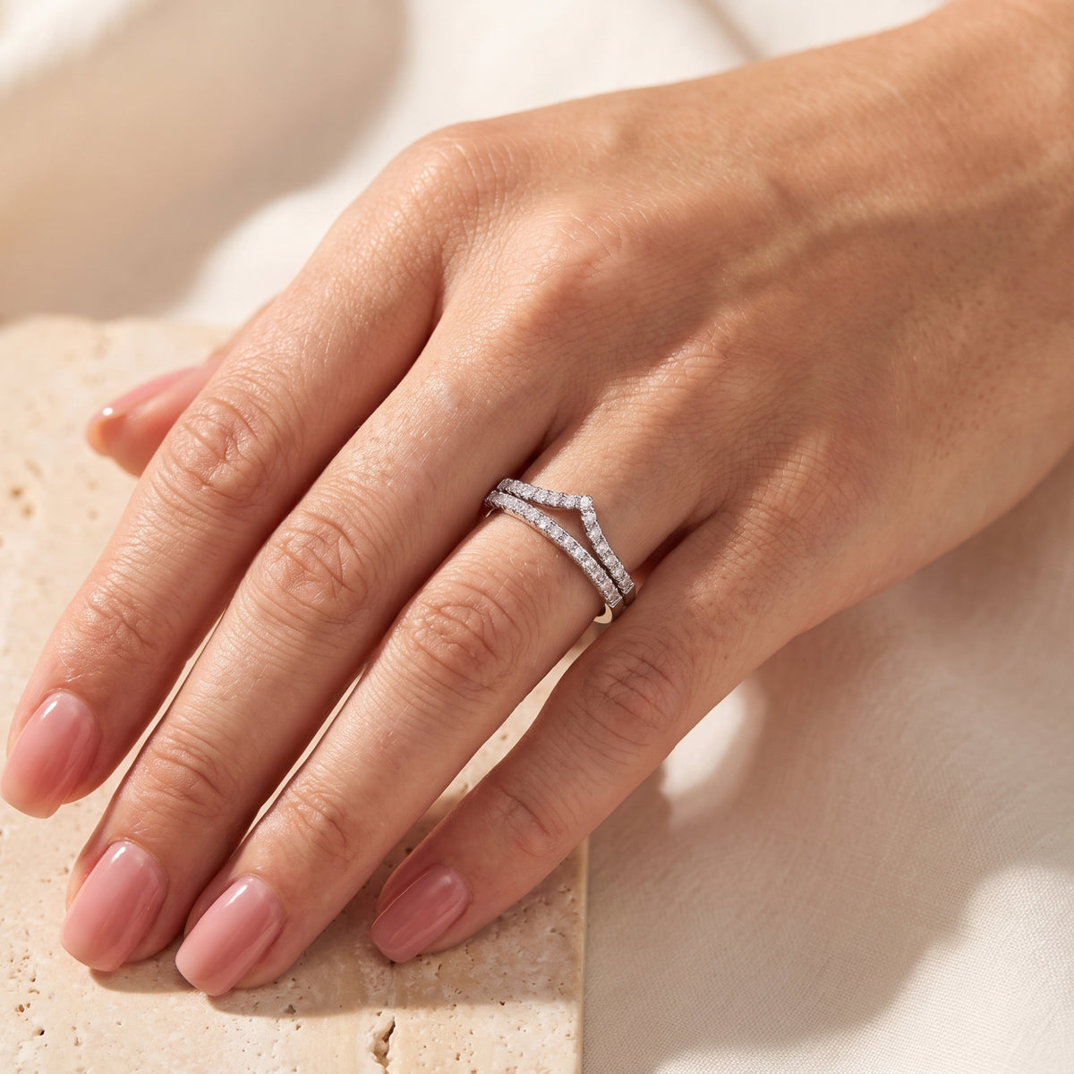 Angled close-up of a hand wearing the silver double chevron ring set on a beige stone slab.