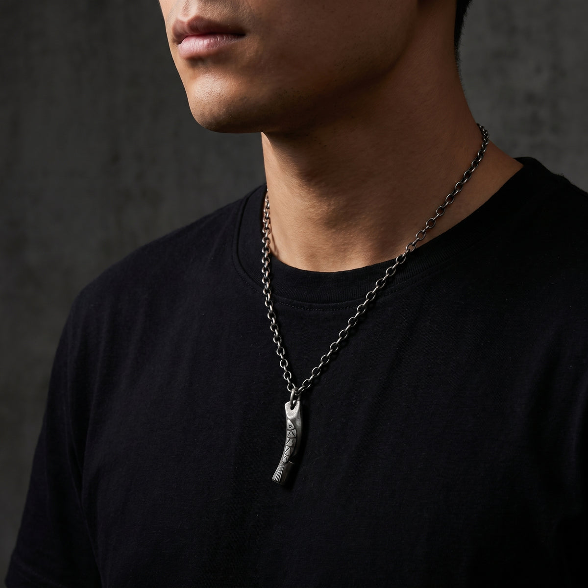 Man wearing the silver carved fish pendant necklace over a plain black T-shirt.