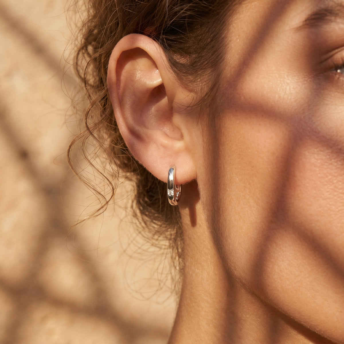 Side profile of a model wearing a white gold huggie hoop earring with a sparkling round moissanite stone.