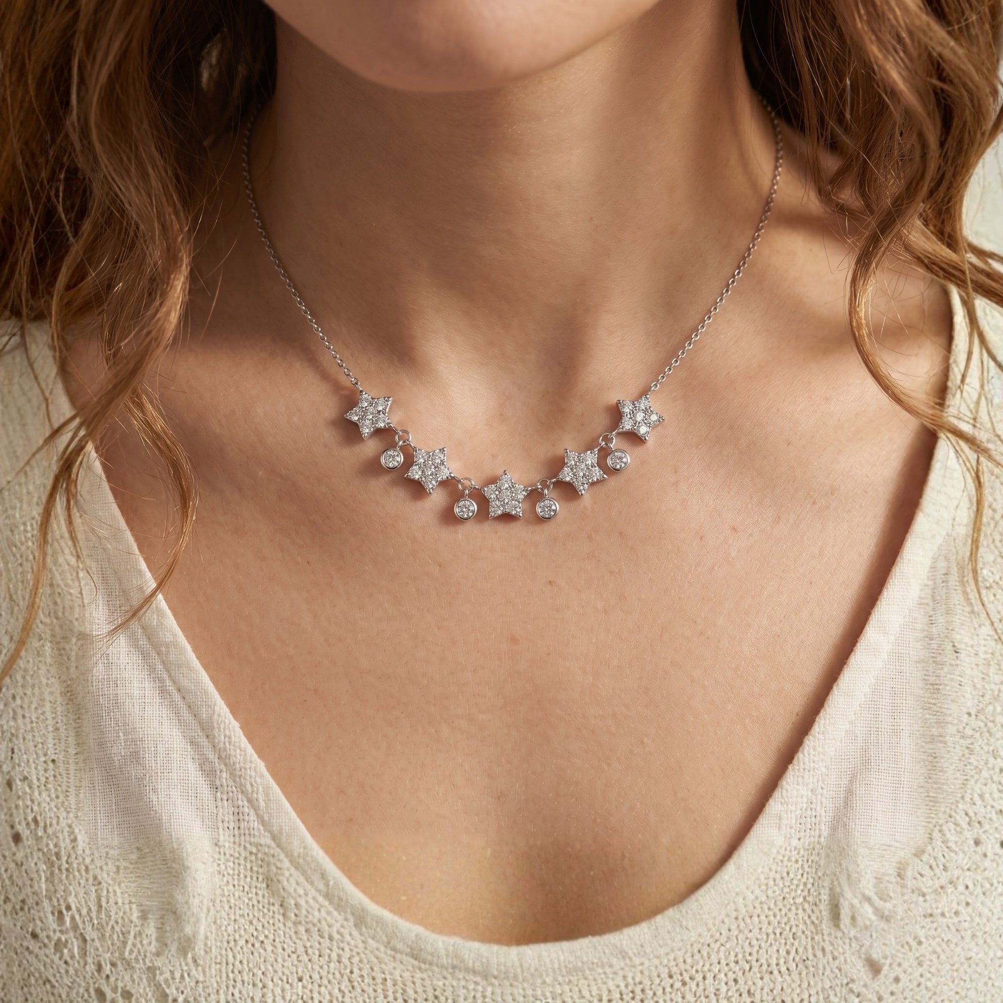 Close-up of a woman wearing the silver Astrielle moissanite necklace featuring five stars and dangling stones.