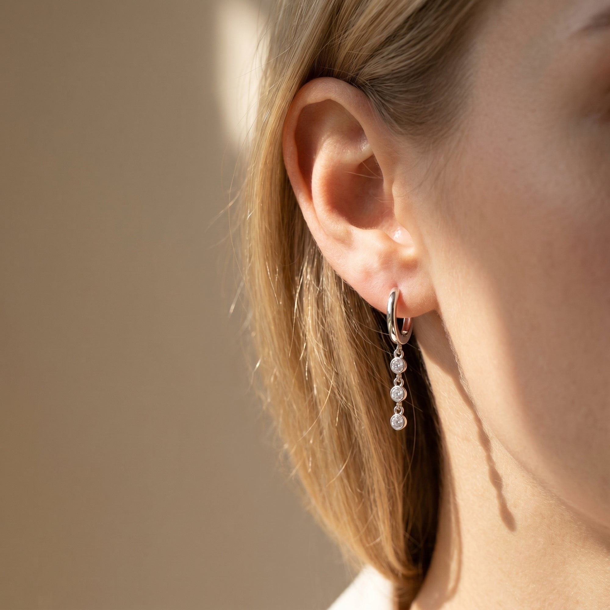 Woman wearing a silver moissanite drop earring with three round stones in bezel settings.