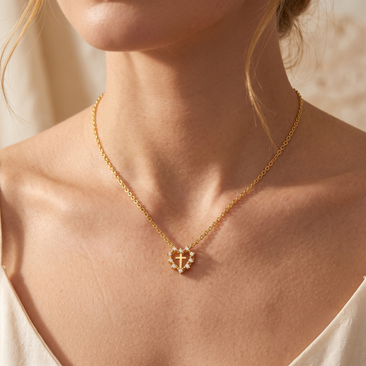 Front-facing view of a model wearing the gold-tone heart halo cross necklace against bare shoulders.