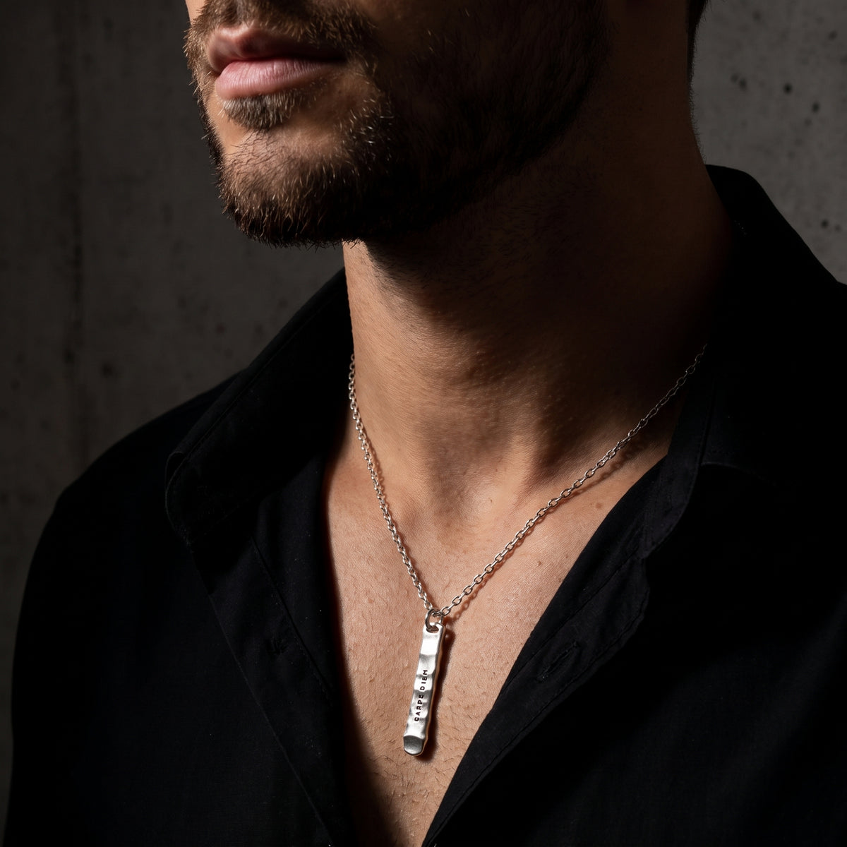 Man wearing the silver CARPE DIEM bar necklace with an open black shirt collar.