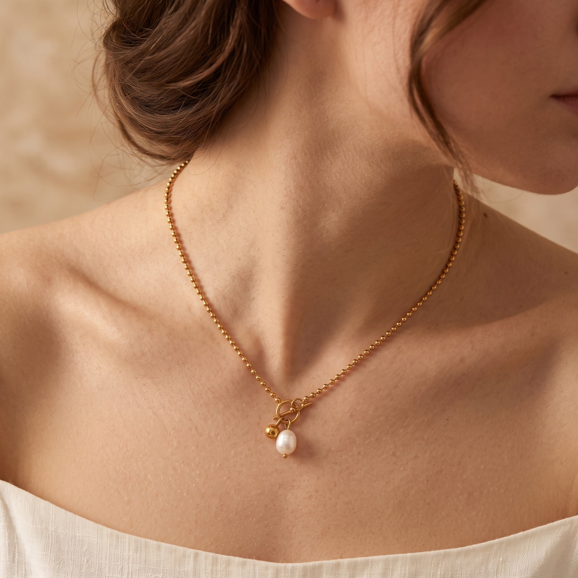 Model wearing the gold ball chain necklace with a baroque pearl and toggle clasp.