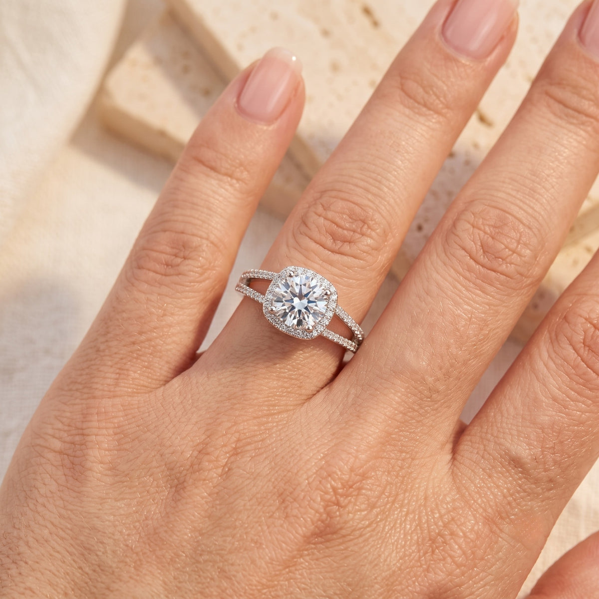 Overhead view of the silver halo ring worn on a hand resting against a cream-colored stone backdrop.