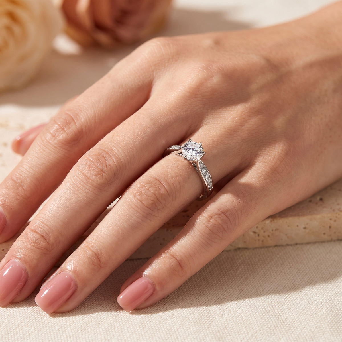 Side-angle hand shot showcasing a round clear solitaire ring with pavé-set accent stones on a finger.