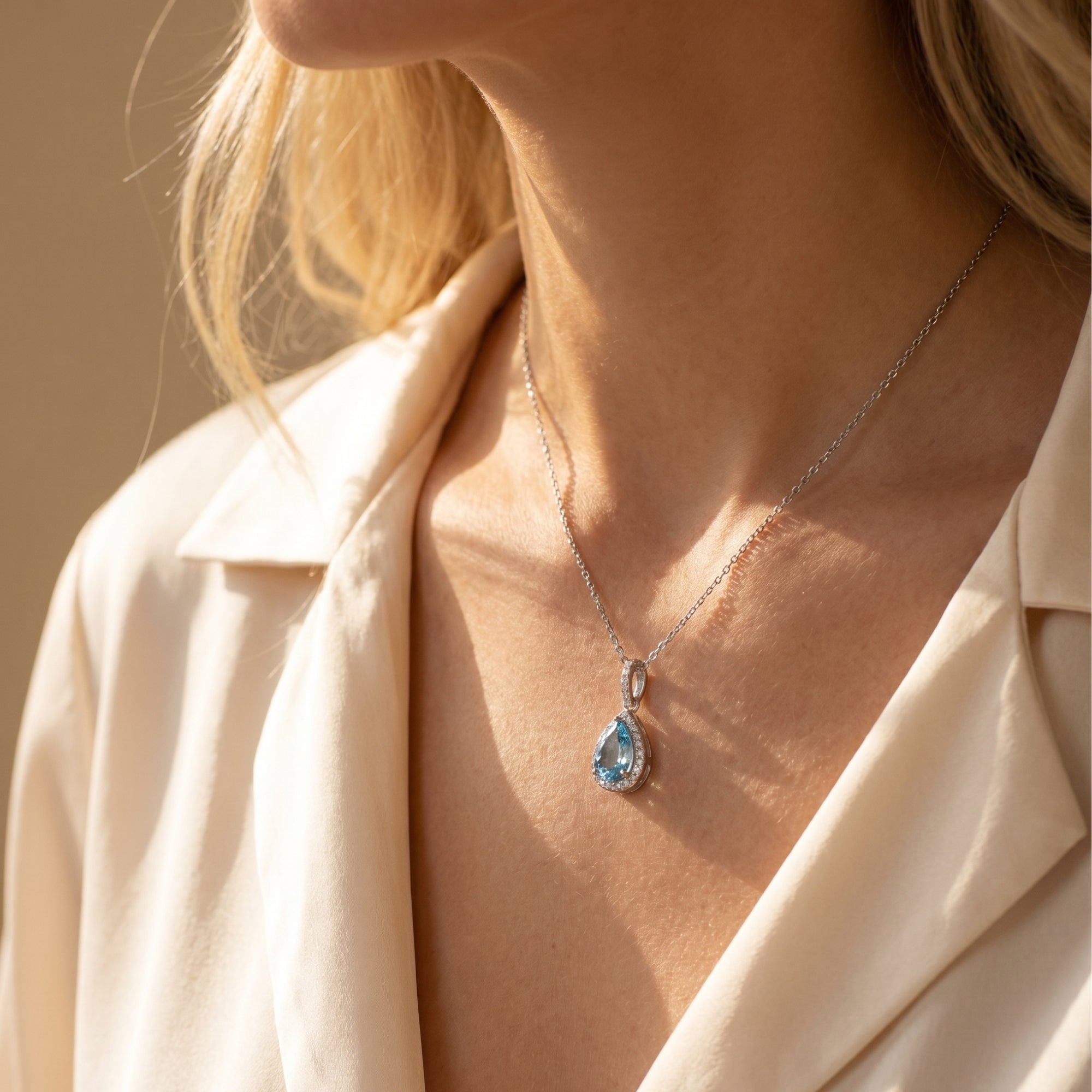 Model wearing the sterling silver pear-shaped aquamarine halo necklace with a cream blouse.