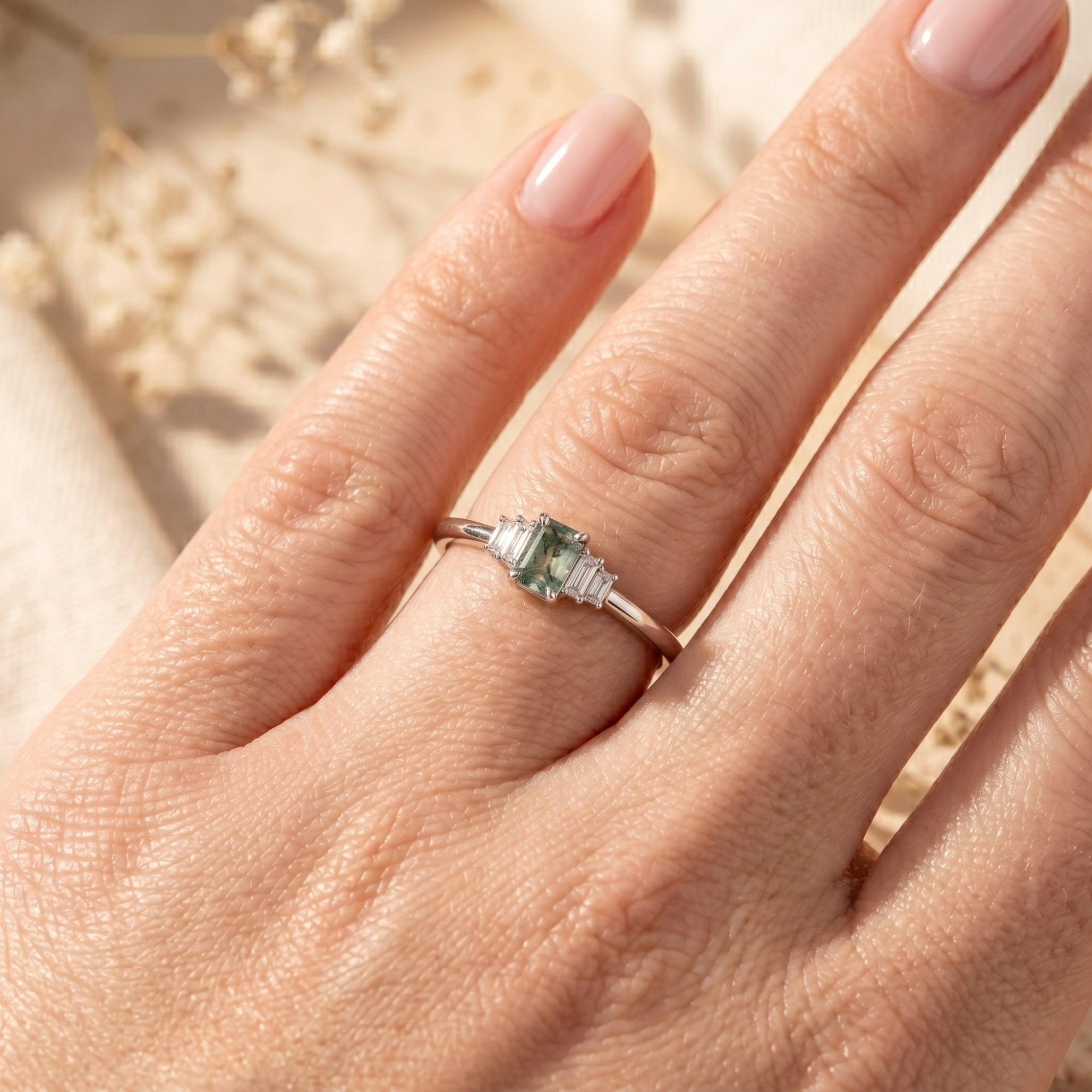 Sterling silver emerald-cut moss agate promise ring with baguette diamonds worn on a hand.