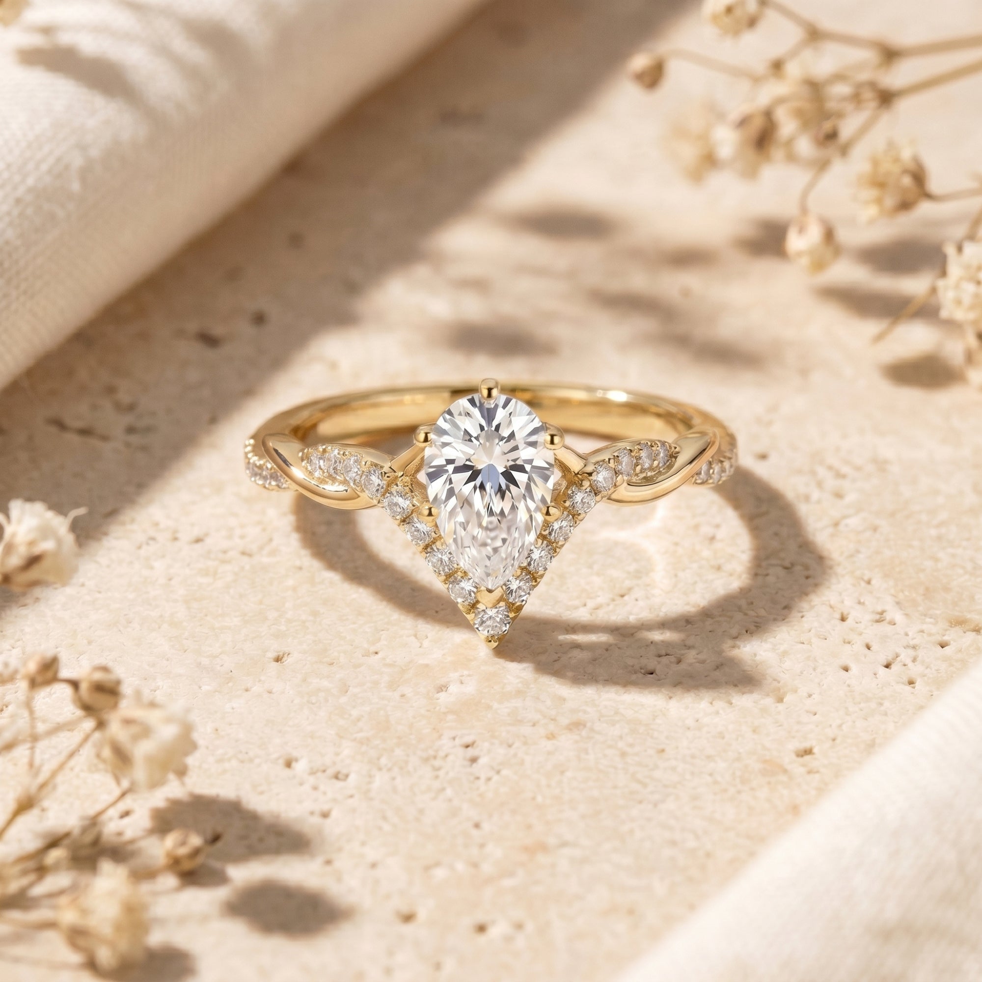 Yellow gold pear-cut moissanite promise ring with a chevron halo and twisted band on a stone surface.