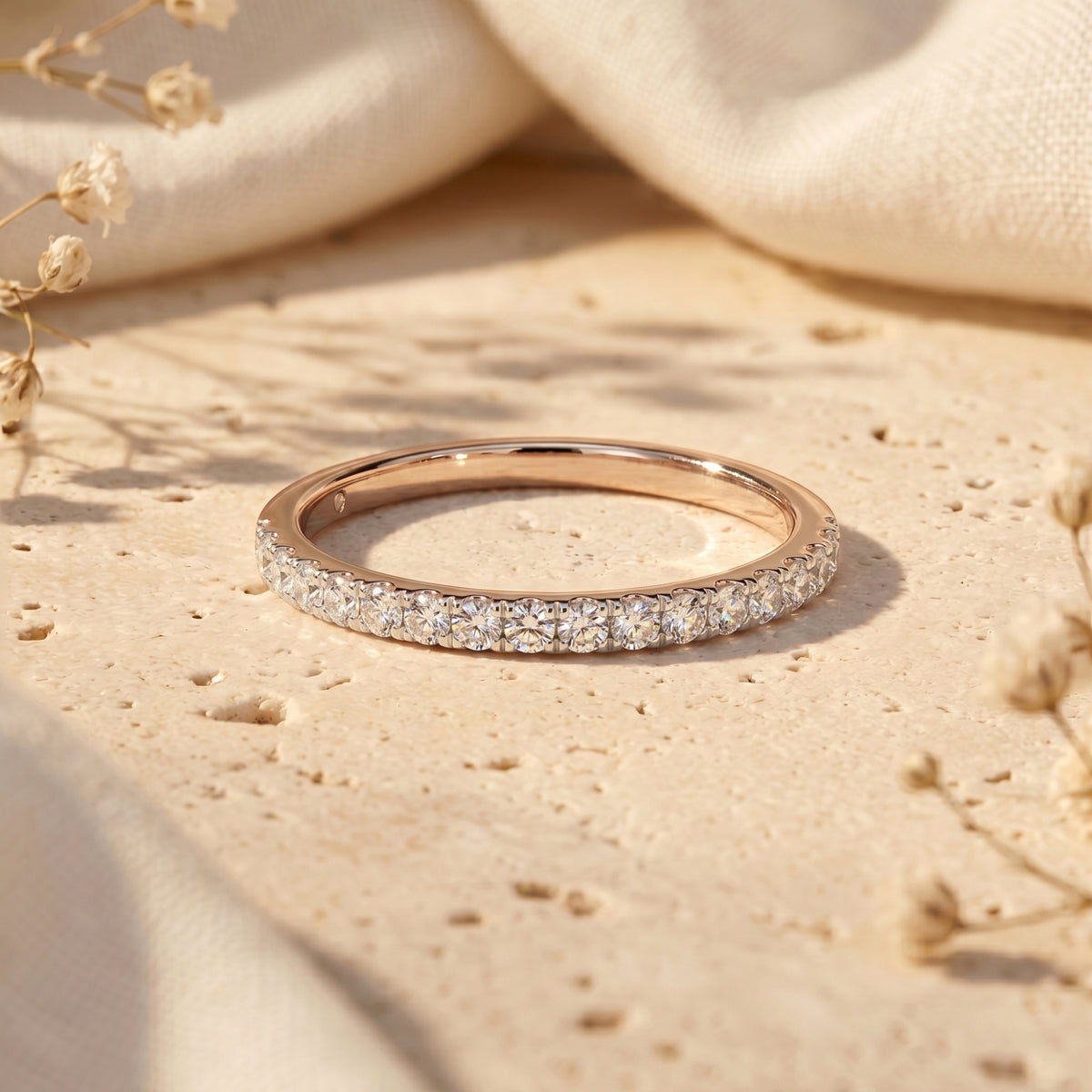 Sylvienne moissanite pave band in rose gold finish displayed on a neutral stone surface.