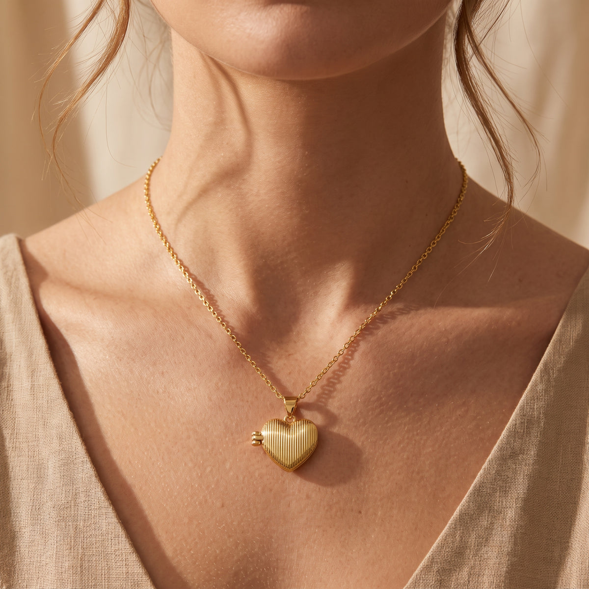 Close-up of a gold-tone ribbed heart locket necklace worn around a model's neck with a V-neck top.
