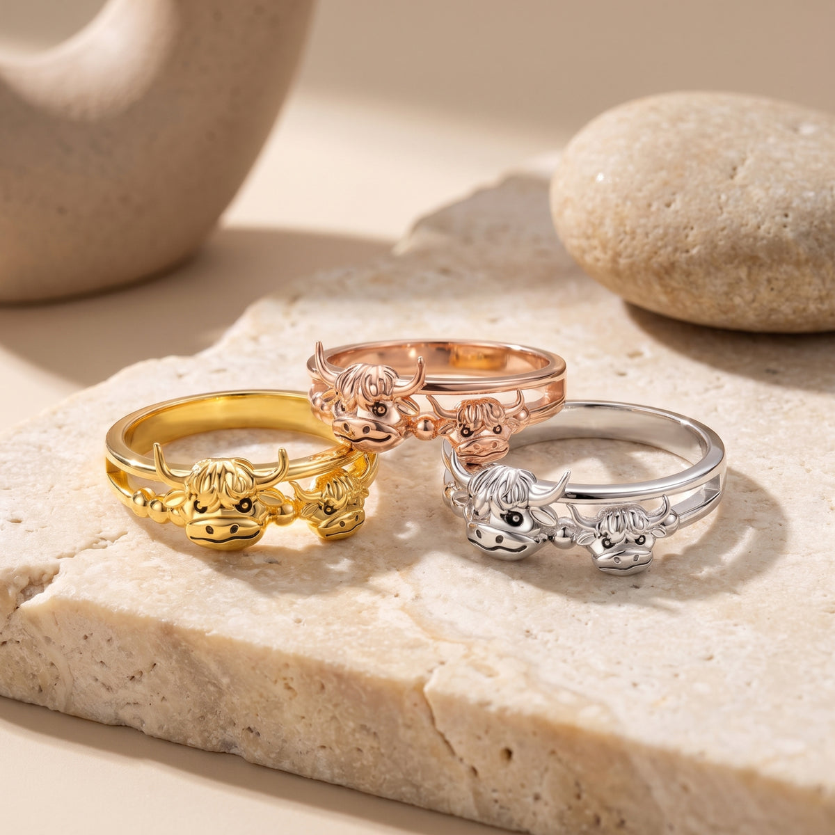 Three highland cow rings in gold-tone, rose gold-tone, and silver-tone finishes, each with mother-and-calf heads.