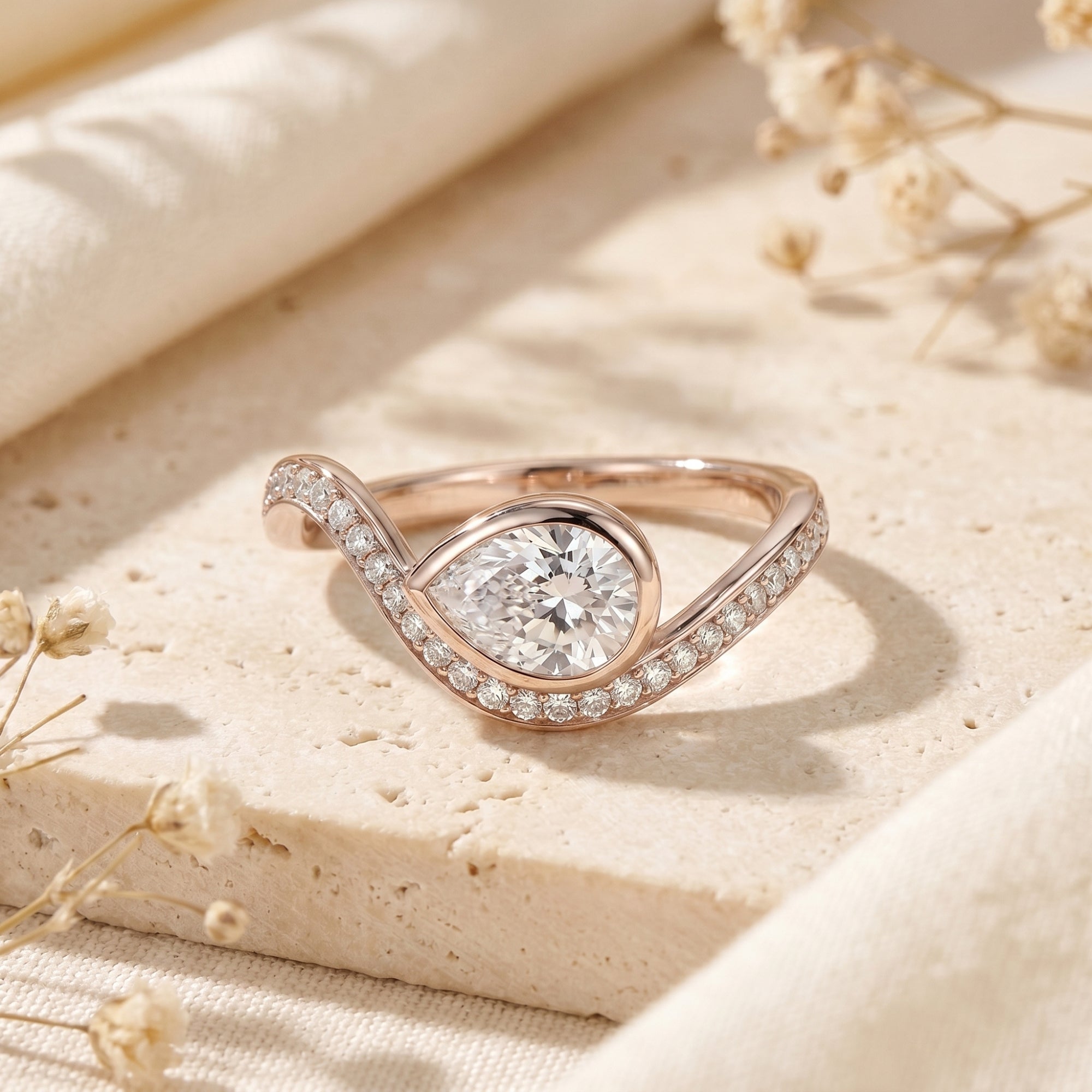 Rose gold pear-cut moissanite bypass ring on a stone background.