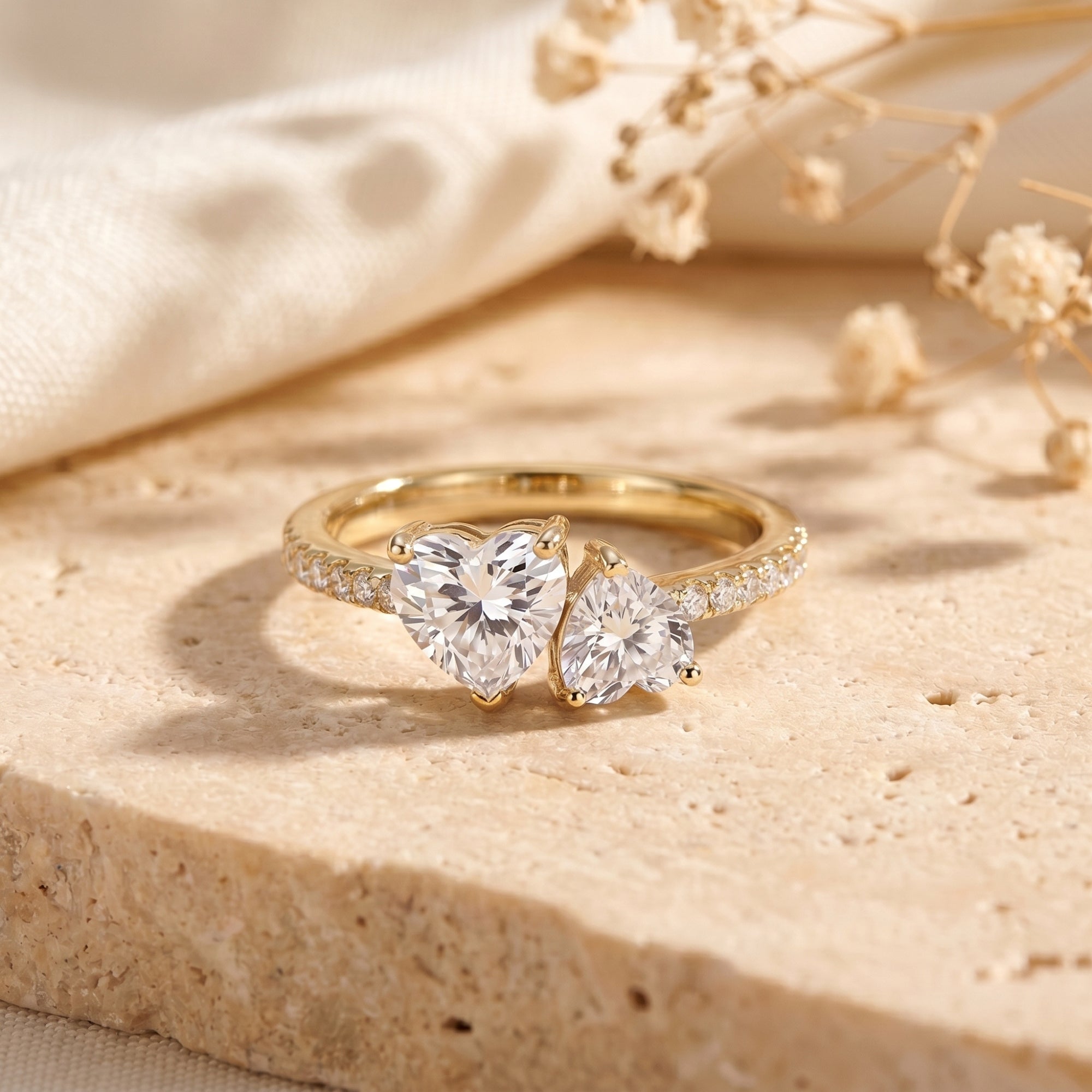 Yellow gold bypass ring with two heart-cut moissanite stones displayed on a stone ledge.