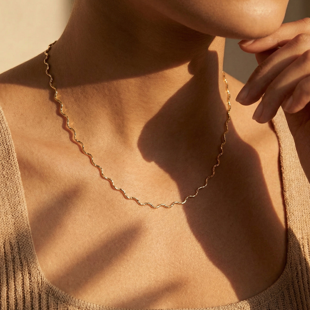 Model wearing the fine gold-toned wavy chain necklace with a ribbed beige scoop-neck top.