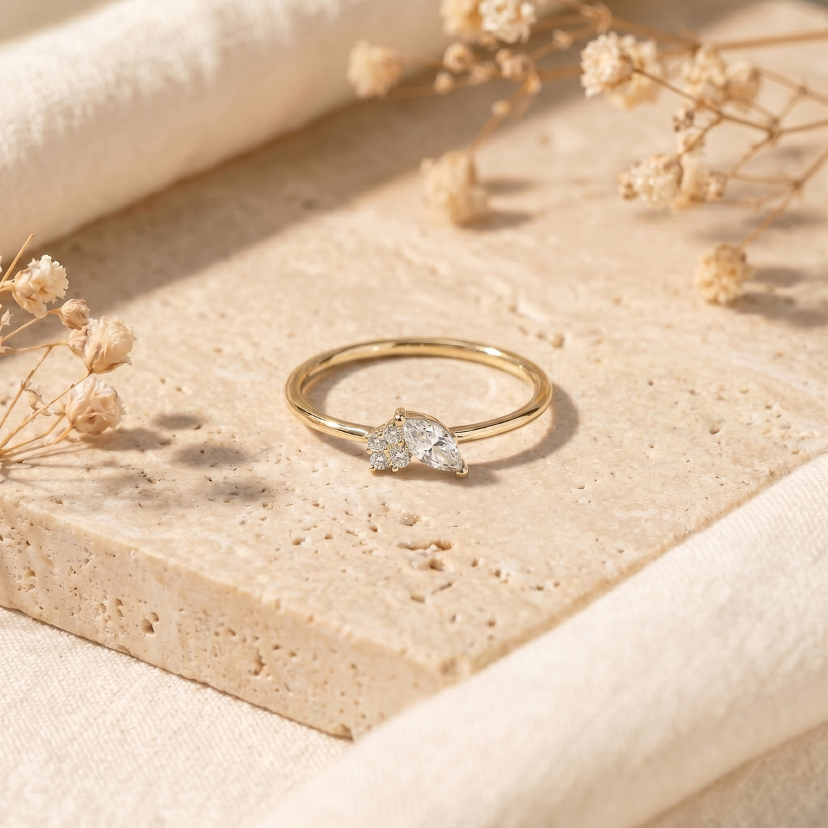 Yellow gold marquise moissanite ring on stone with dried flowers.