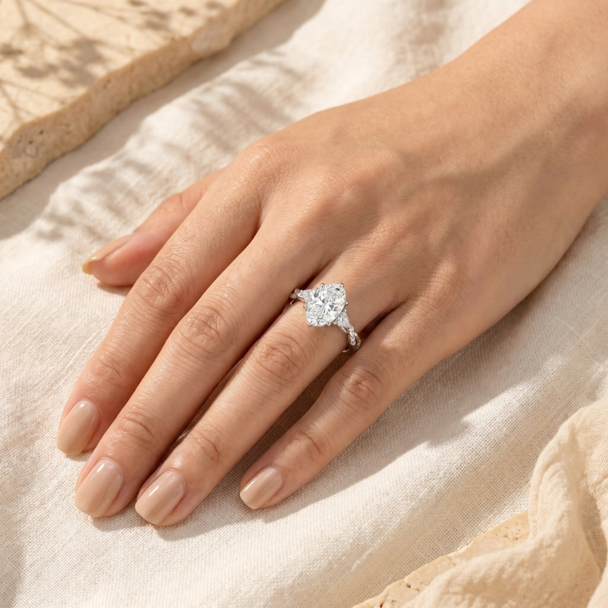 Woman wearing an oval moissanite ring in solid gold on her hand against a neutral fabric.