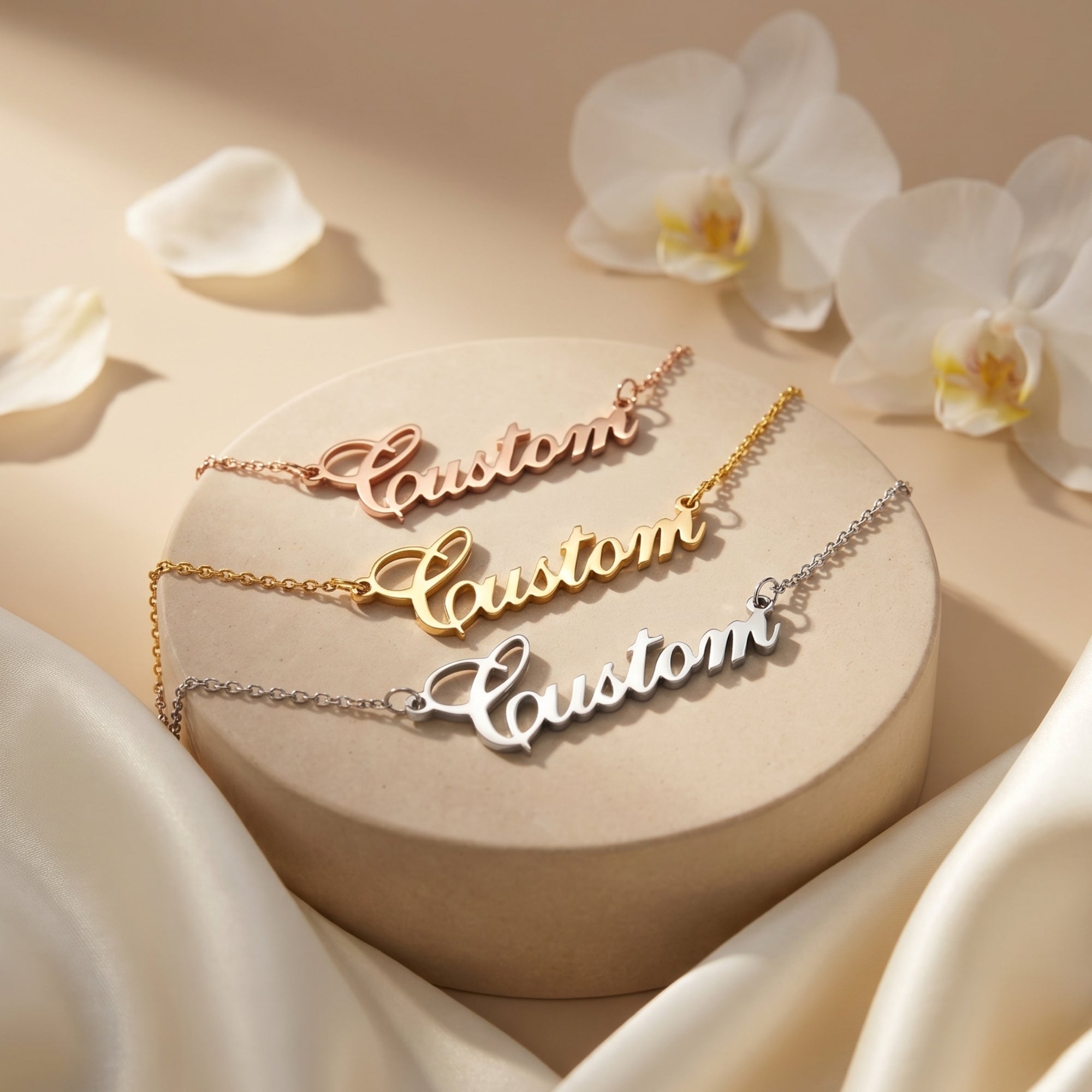 Three personalized name necklaces in rose gold, 18K gold, and silver finishes on a beige display stand.