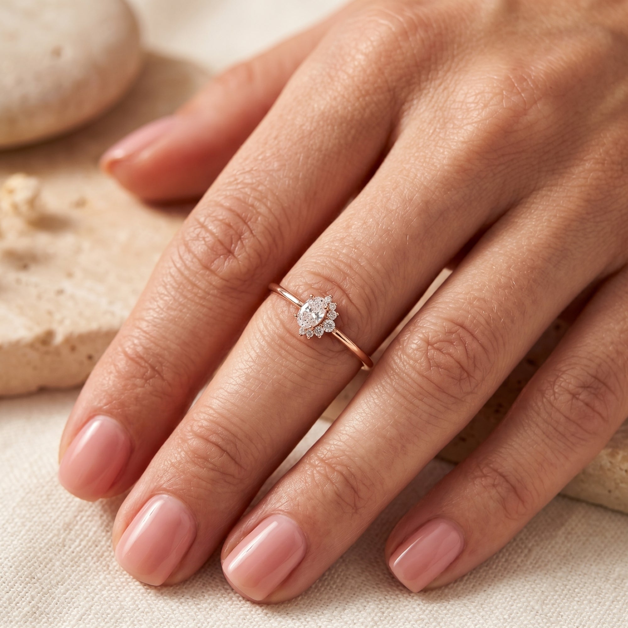 Rose gold 2CT oval moissanite ring worn on a finger to demonstrate the asymmetric cluster design.