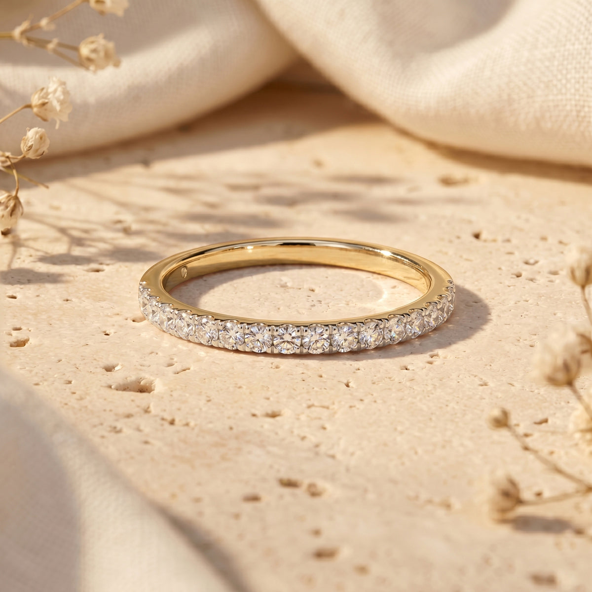 Yellow gold Sylvienne moissanite pave band ring resting on a textured surface with soft floral accents.