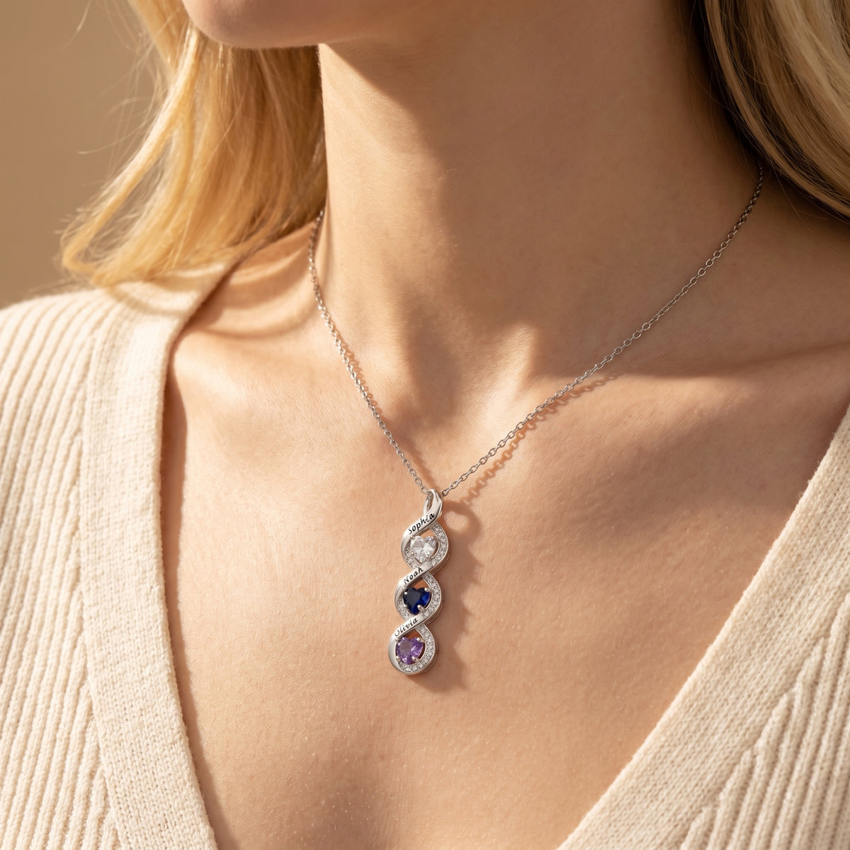 Model wearing a silver Anatolia infinity necklace featuring personalized names and heart stones.