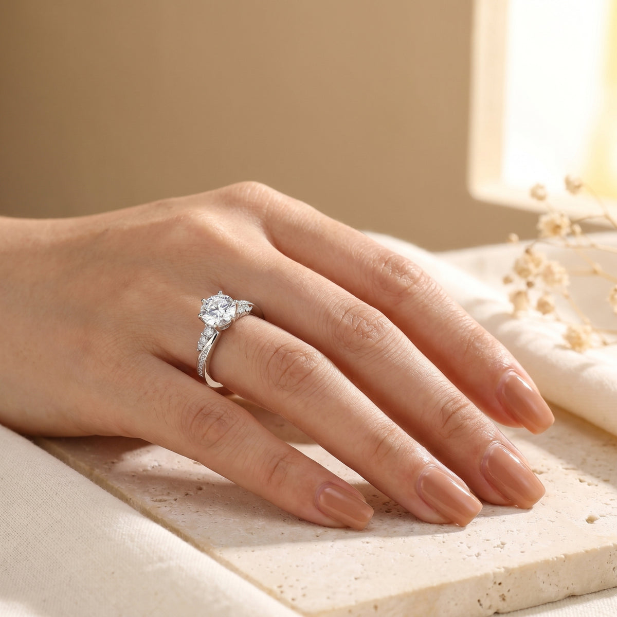 Sterling silver Nicolette moissanite ring on a woman's finger, resting on a stone surface.