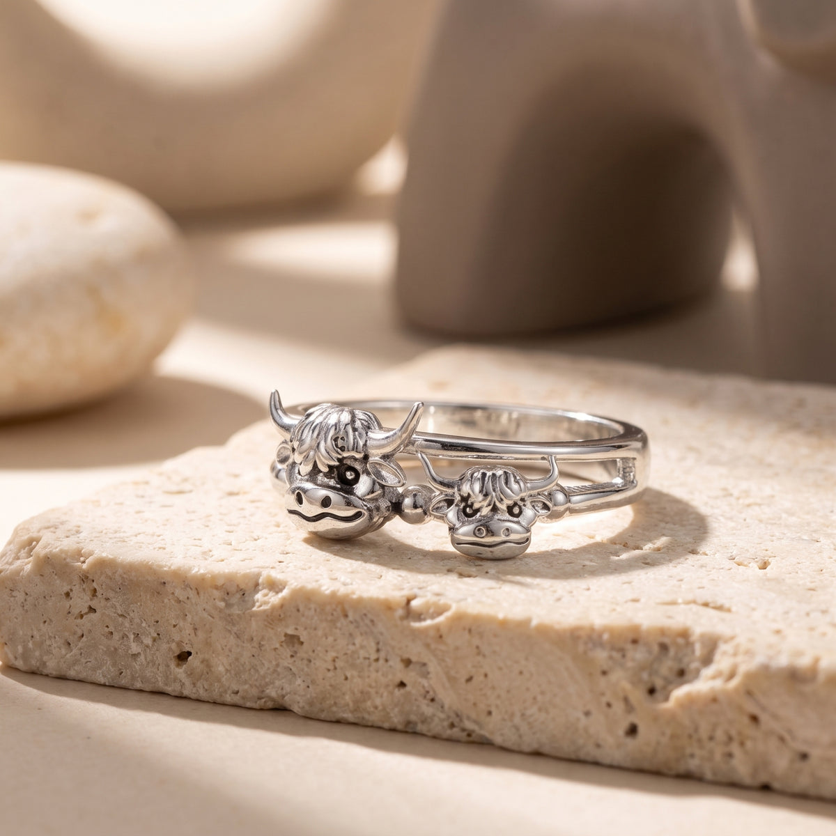 Front view of an all-silver-tone highland cow ring with matching mother-and-calf heads on a stone surface.