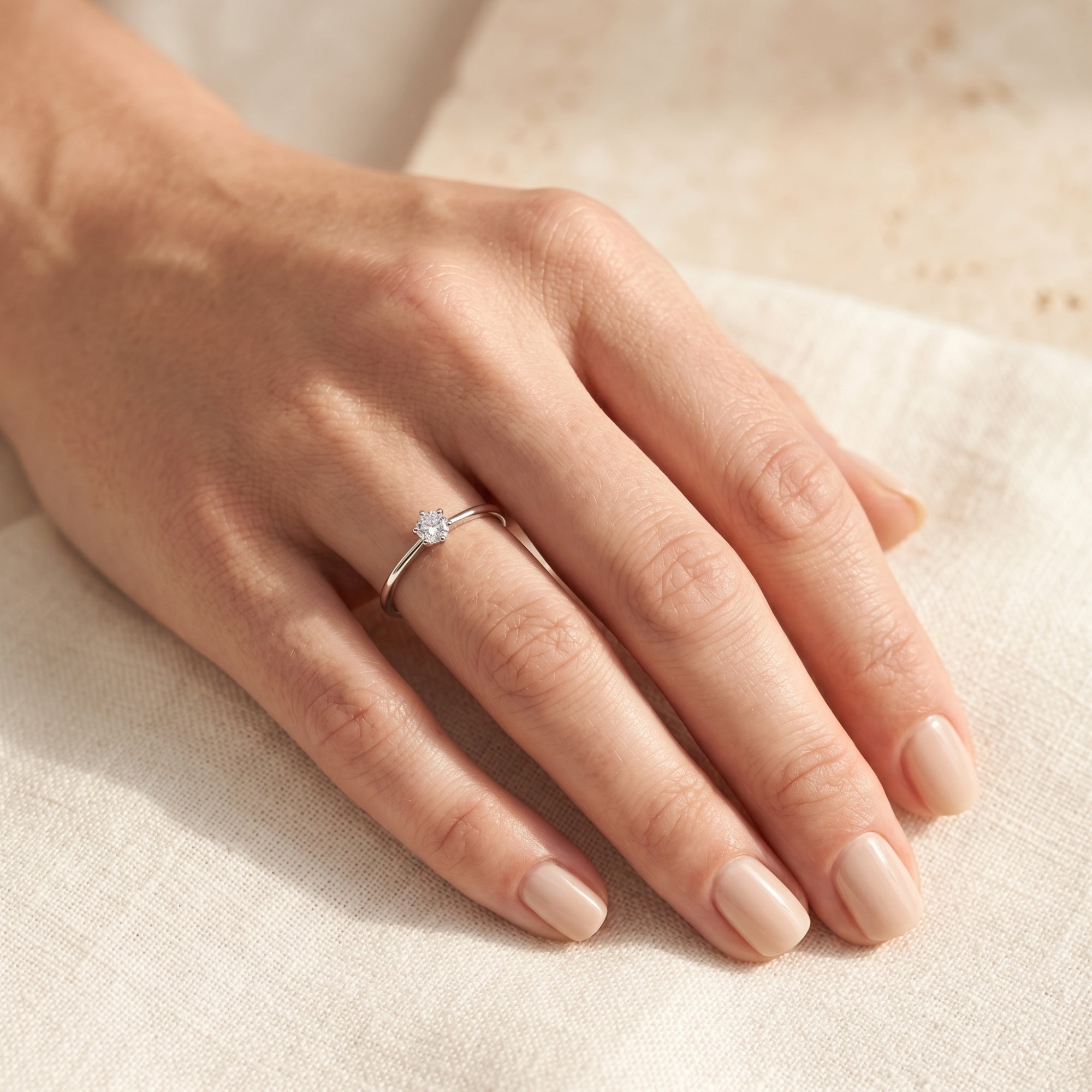 Silver round moissanite engagement ring on a finger for scale.