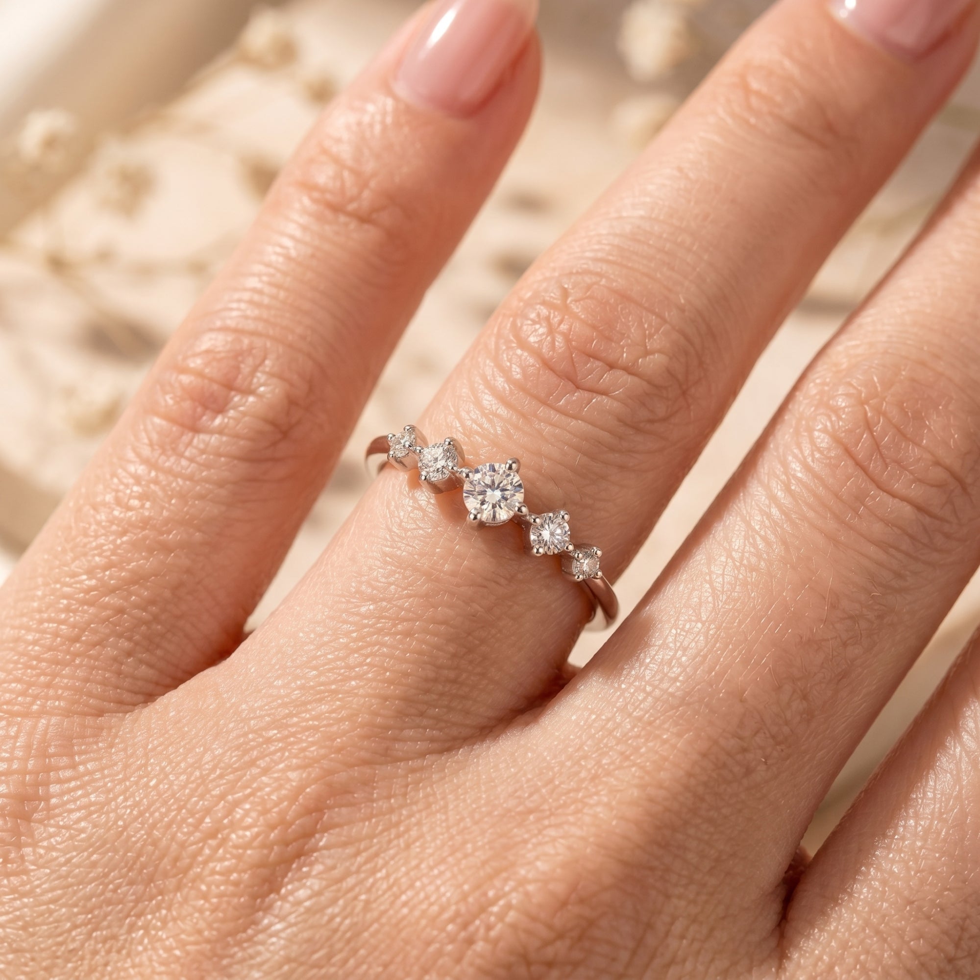 Close-up of silver ring with five round moissanite stones on a hand.