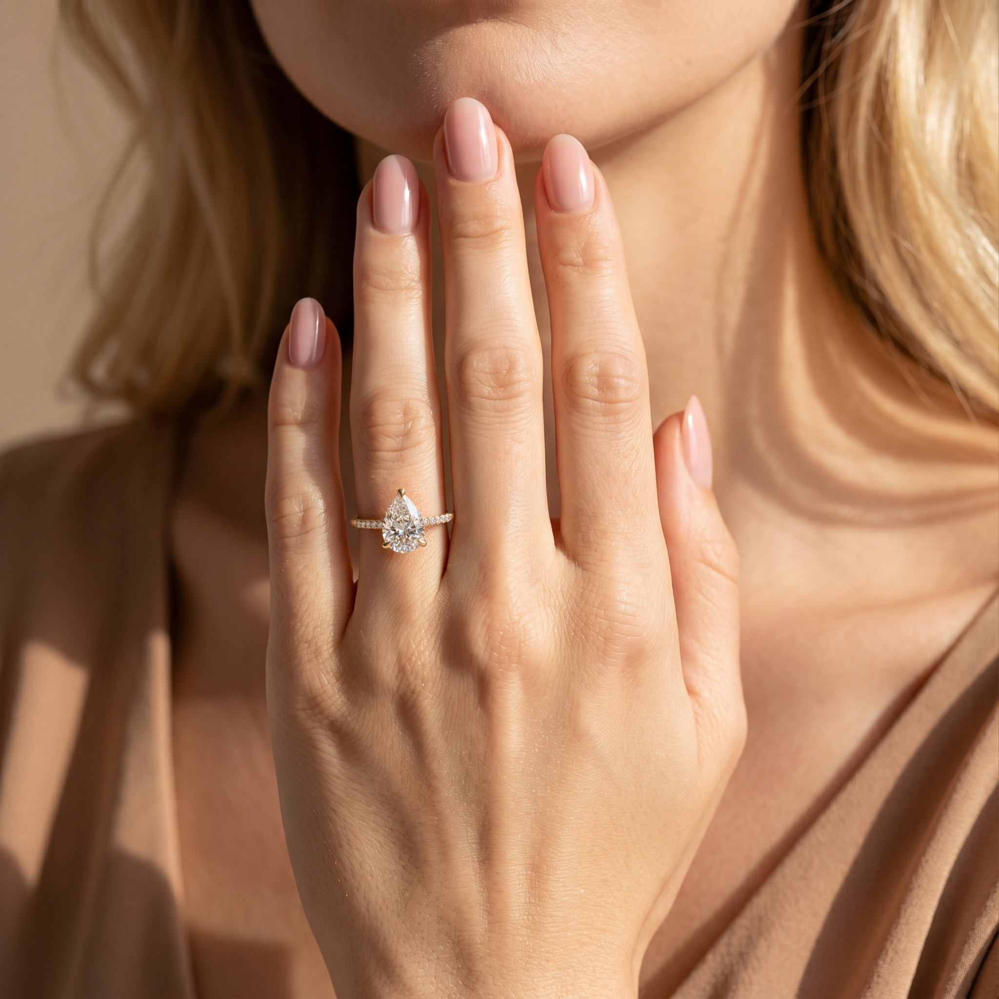 A model showcasing a yellow gold pear-shaped moissanite engagement ring with her hand raised to her chin.