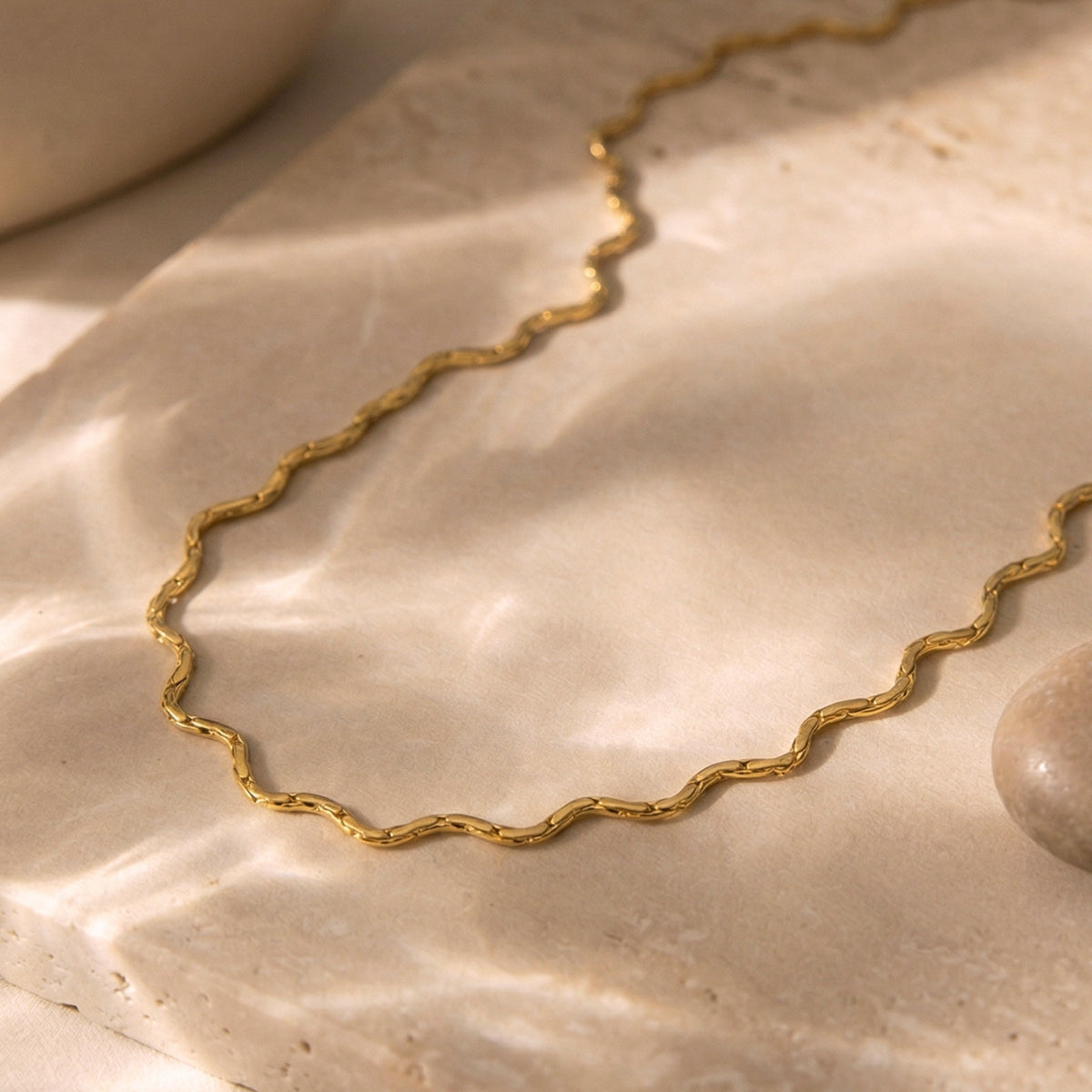Gold-toned wavy chain necklace arranged on a softly textured beige surface.