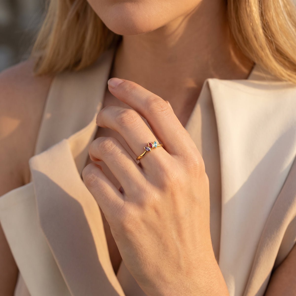 Gold-tone ring with three marquise-cut purple, red, and blue stones worn on a hand.