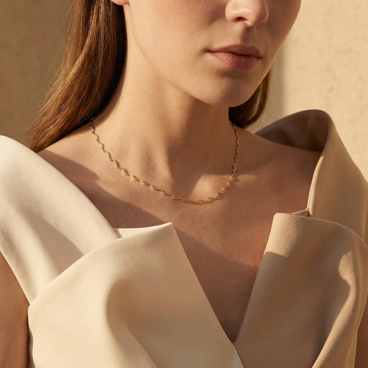 Model wearing a gold-toned wavy chain necklace across her collarbone, cropped from the lower face to chest.