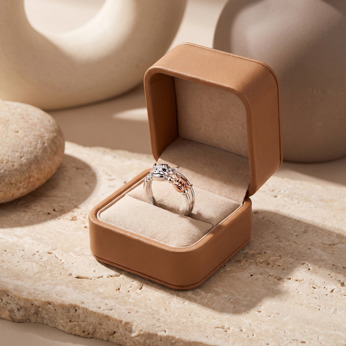 Highland cow and calf ring displayed upright in an open tan jewelry box on a light stone slab.