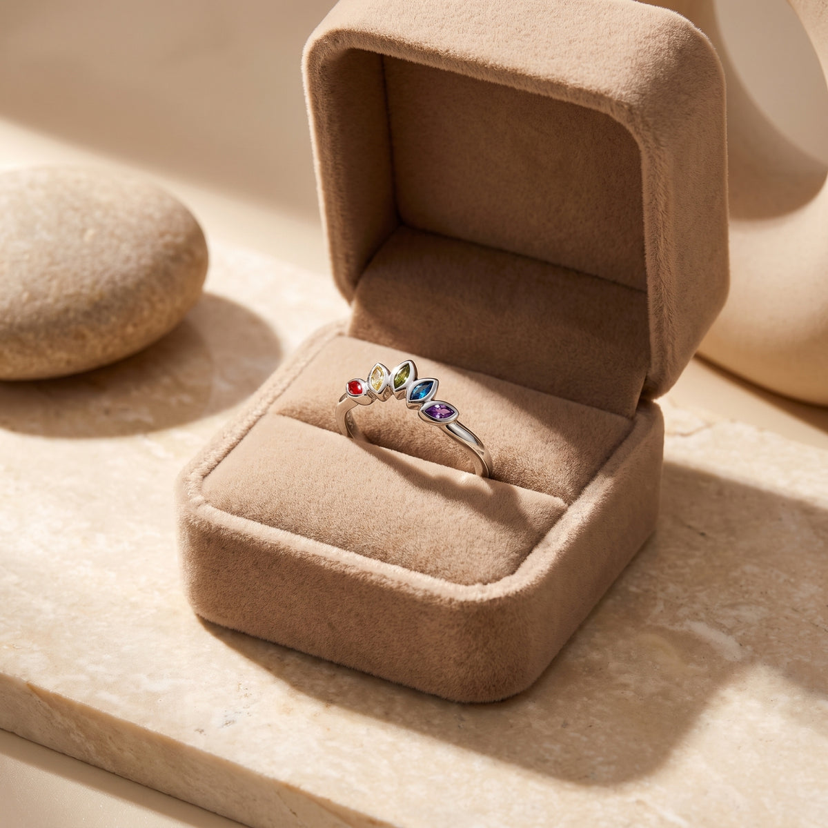 Silver ring with five colorful marquise stones displayed in an open beige velvet jewelry box.