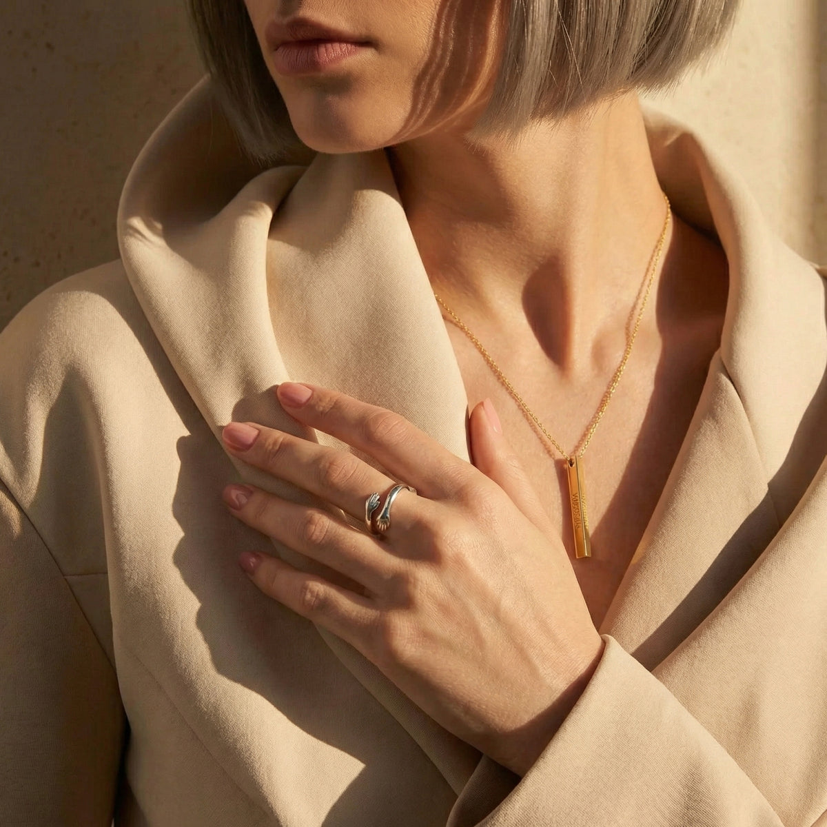 Model wearing the silver hug ring while resting her hand over a beige coat, with a bar pendant necklace visible.