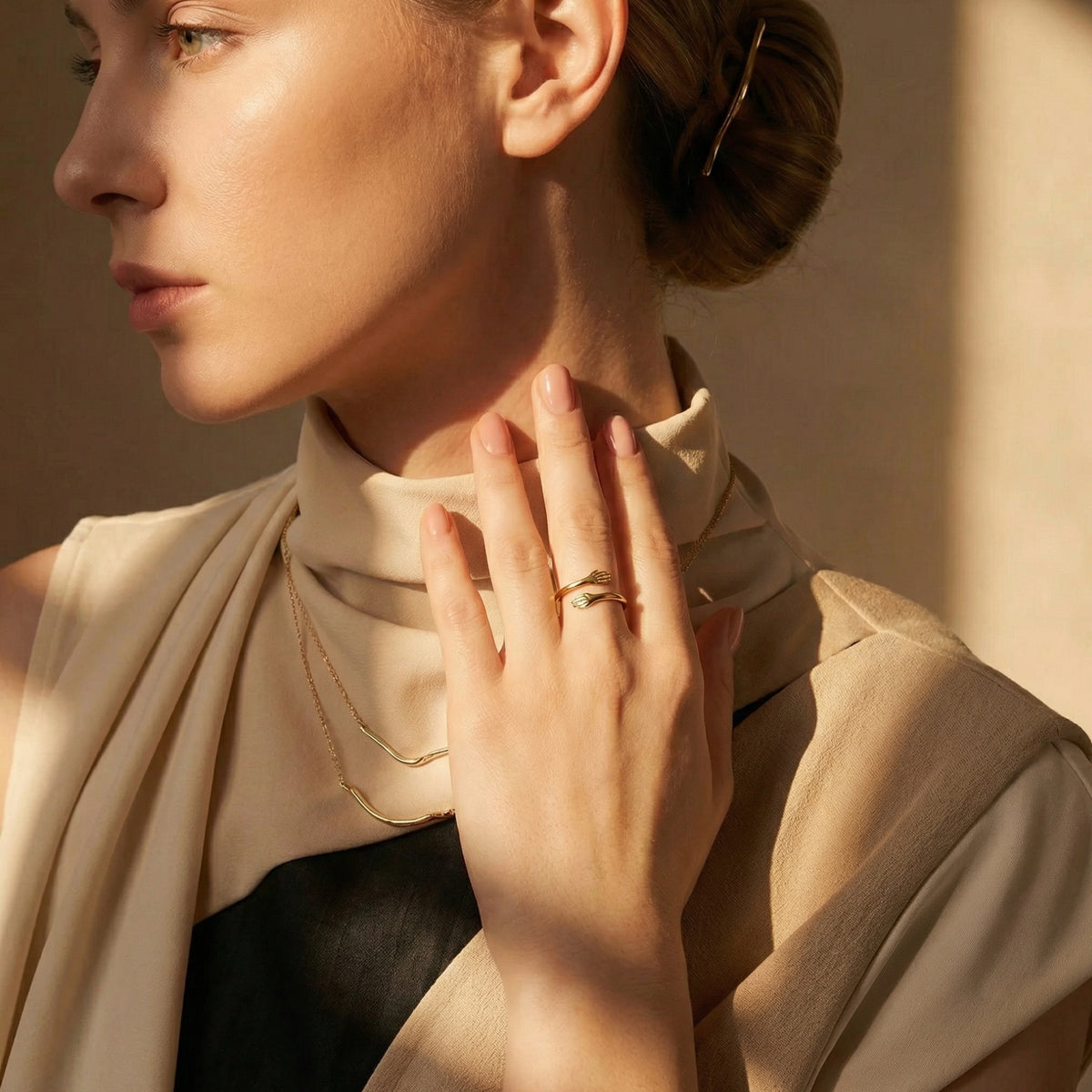 Woman wearing the gold-colored hug ring on her middle finger, with her hand raised near her neck.