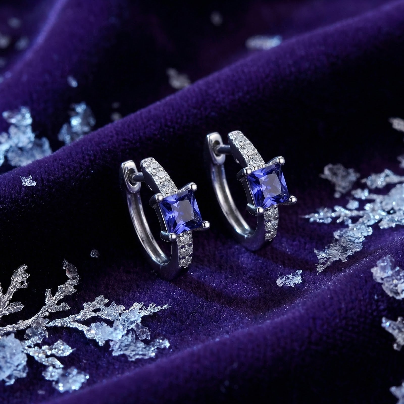 Sterling silver hoop earrings with square-cut simulated tanzanite on purple velvet with snowflake accents.