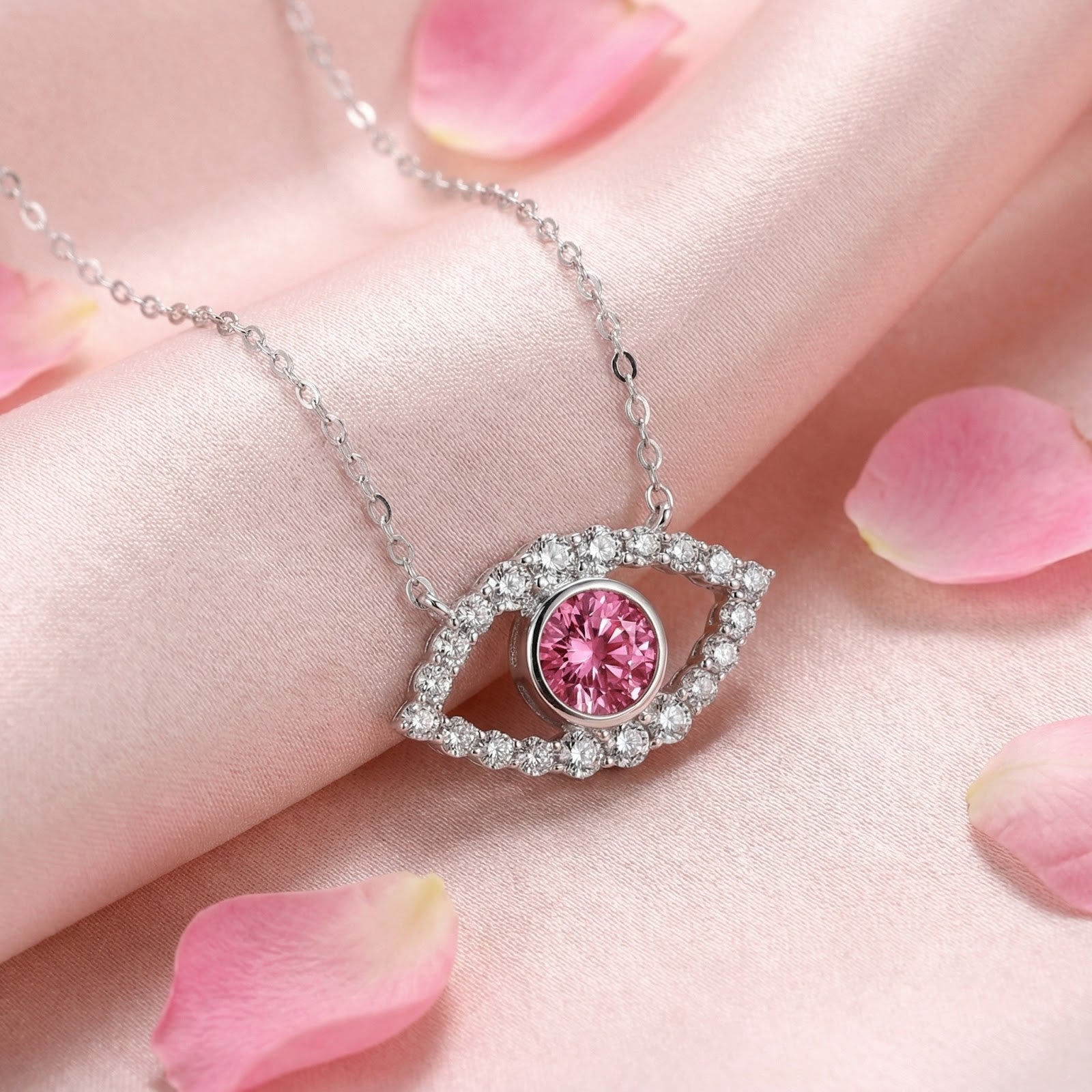 Pink moissanite eye necklace in sterling silver on pink satin fabric with rose petals.