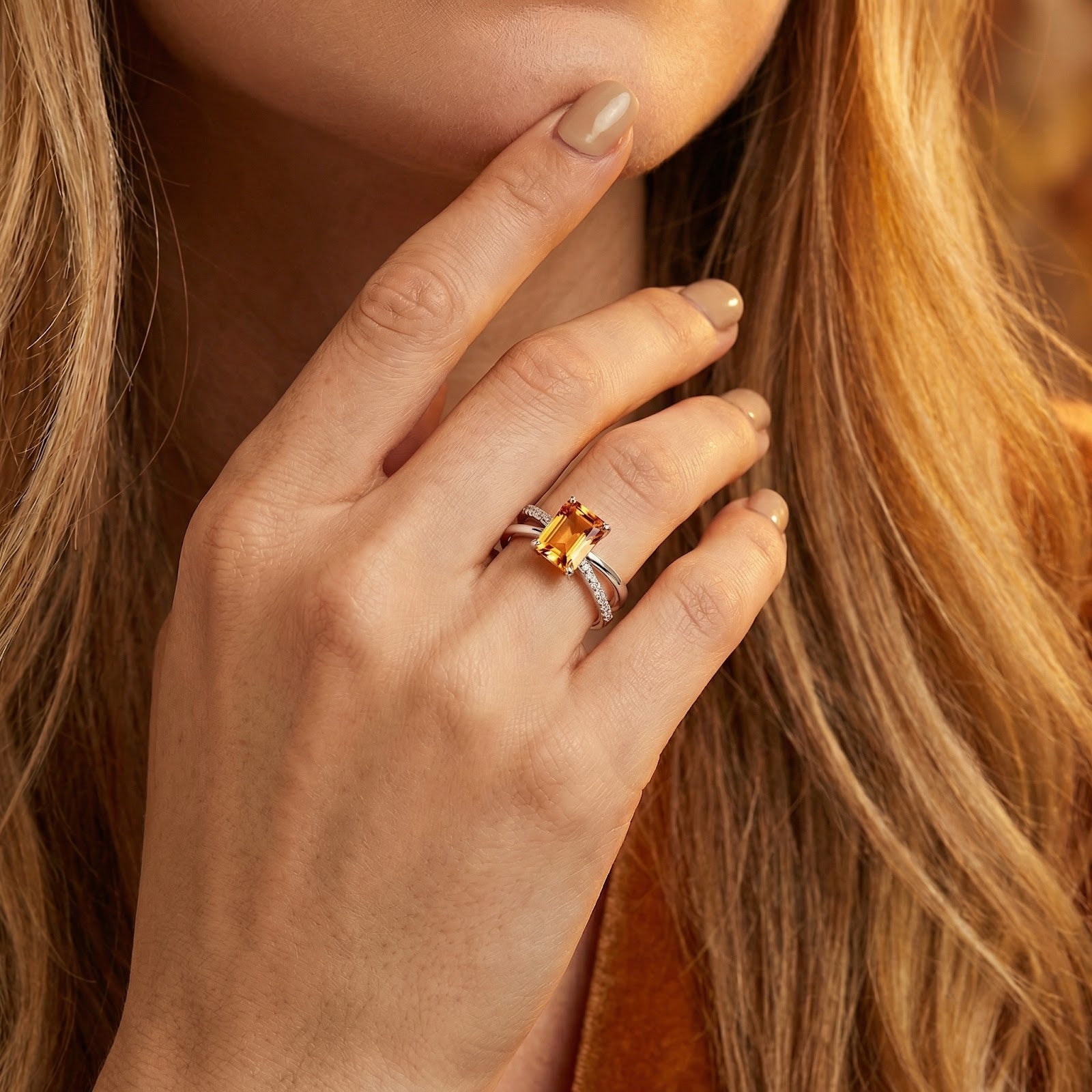 Close-up of the honeyed simulated topaz twist ring in S925 sterling silver on a model's finger touching her chin.