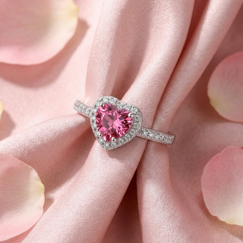 Top-down view of the heart-cut simulated pink tourmaline sterling silver halo ring on pink fabric.