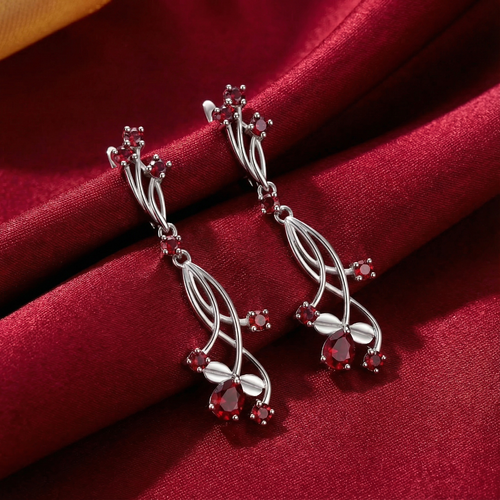 Sterling silver Valisara drop earrings with round and pear-cut simulated rubies on a red silk background.