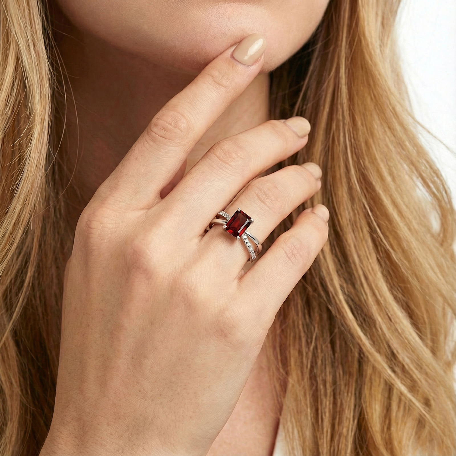 Close-up of the S925 sterling silver Isolt twist ring with a red emerald cut garnet worn on a finger.