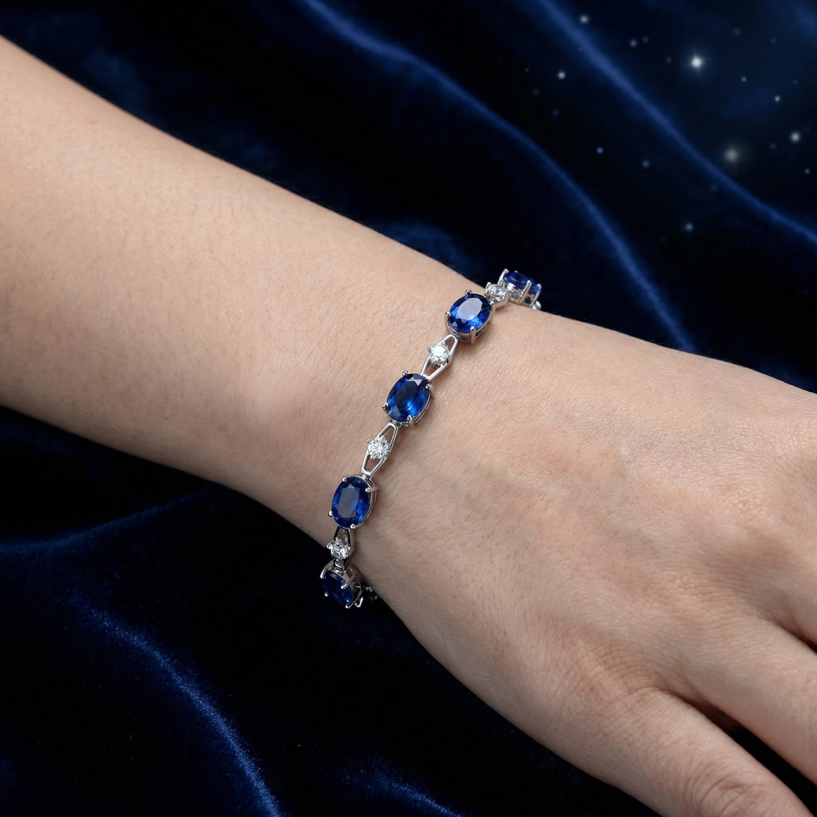 Close-up view of the sterling silver bracelet with oval-cut simulated blue sapphires on a woman's wrist.