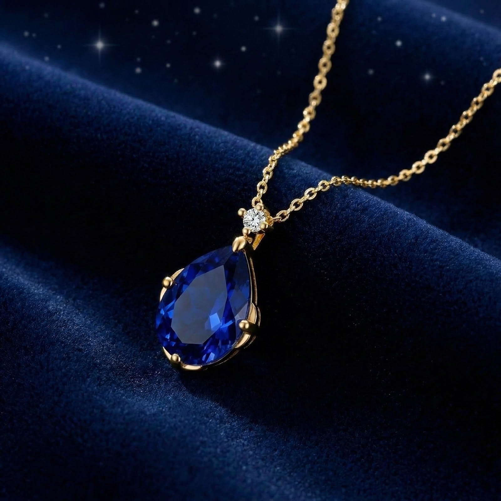 Pear-cut simulated sapphire necklace in 18K gold vermeil resting on deep blue velvet fabric.