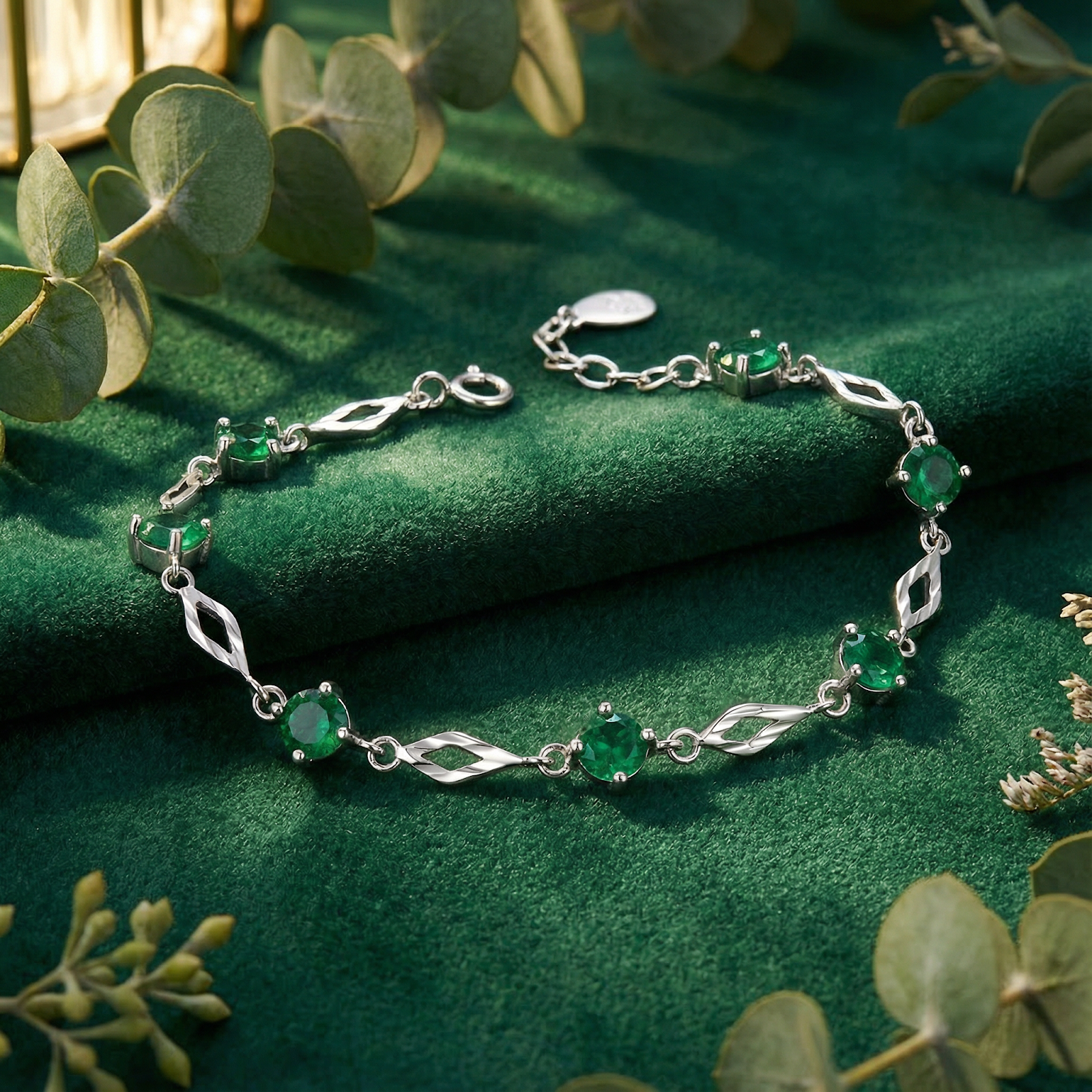 Sterling silver station bracelet with round simulated emeralds on green velvet with eucalyptus leaves.