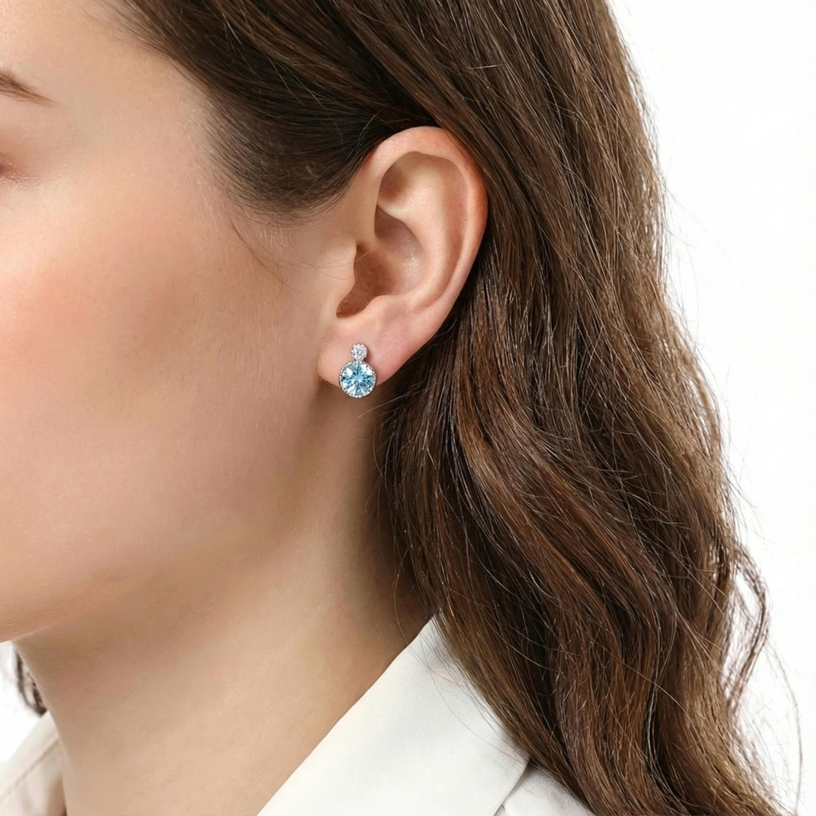 Brunette woman wearing a round-cut simulated aquamarine and sterling silver stud earring on her ear.